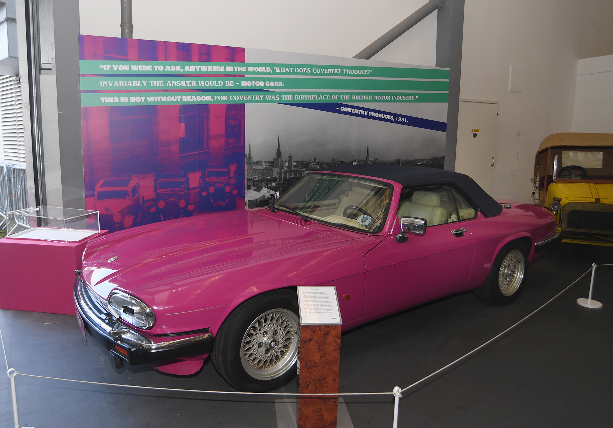 The iconic pink Barbie Jaguar. A display board behind it features archive imagery and a quote from Coventry Produces in 1951, "If you were to ask, anywhere in the world, 'What does Coventry produce?' the answer would invariably be - motor cars. This is not without reason, for Coventry was the birthplace of the British motor industry."