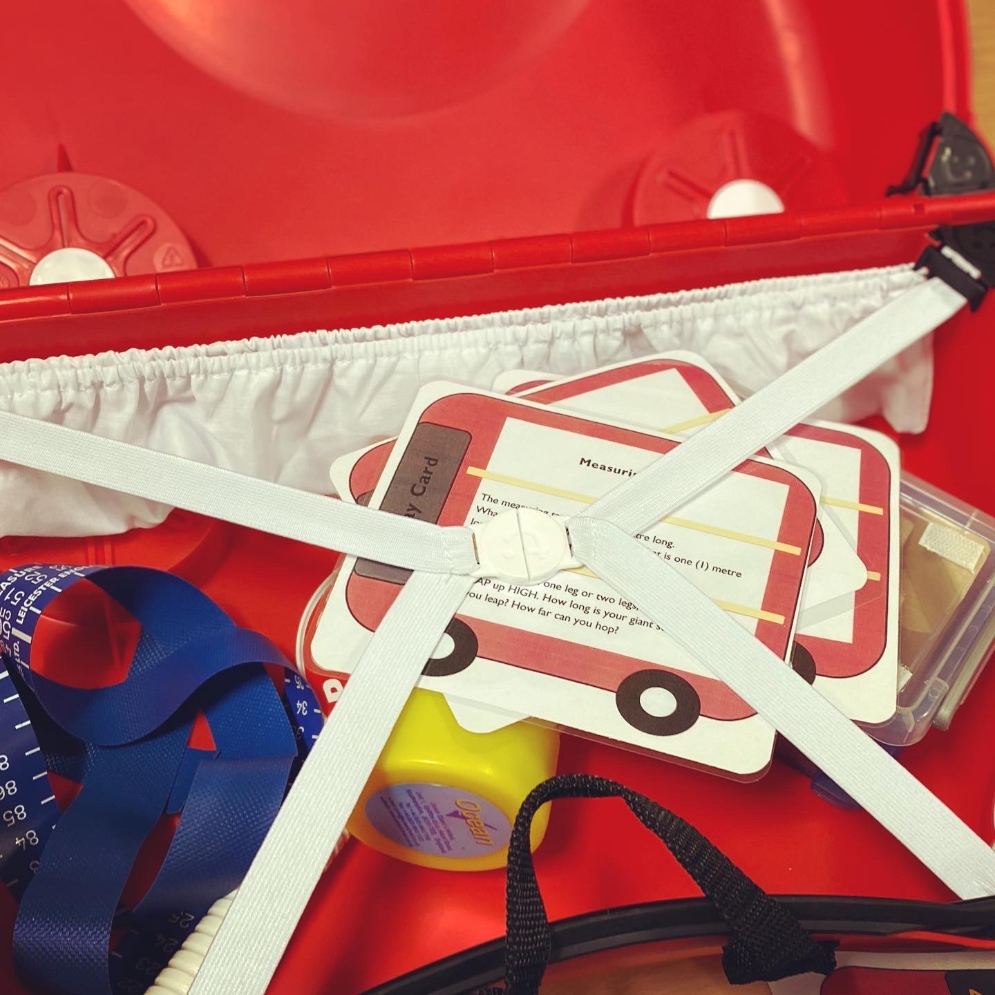 A photograph of a red trail box containing a measuring tape and activity cards