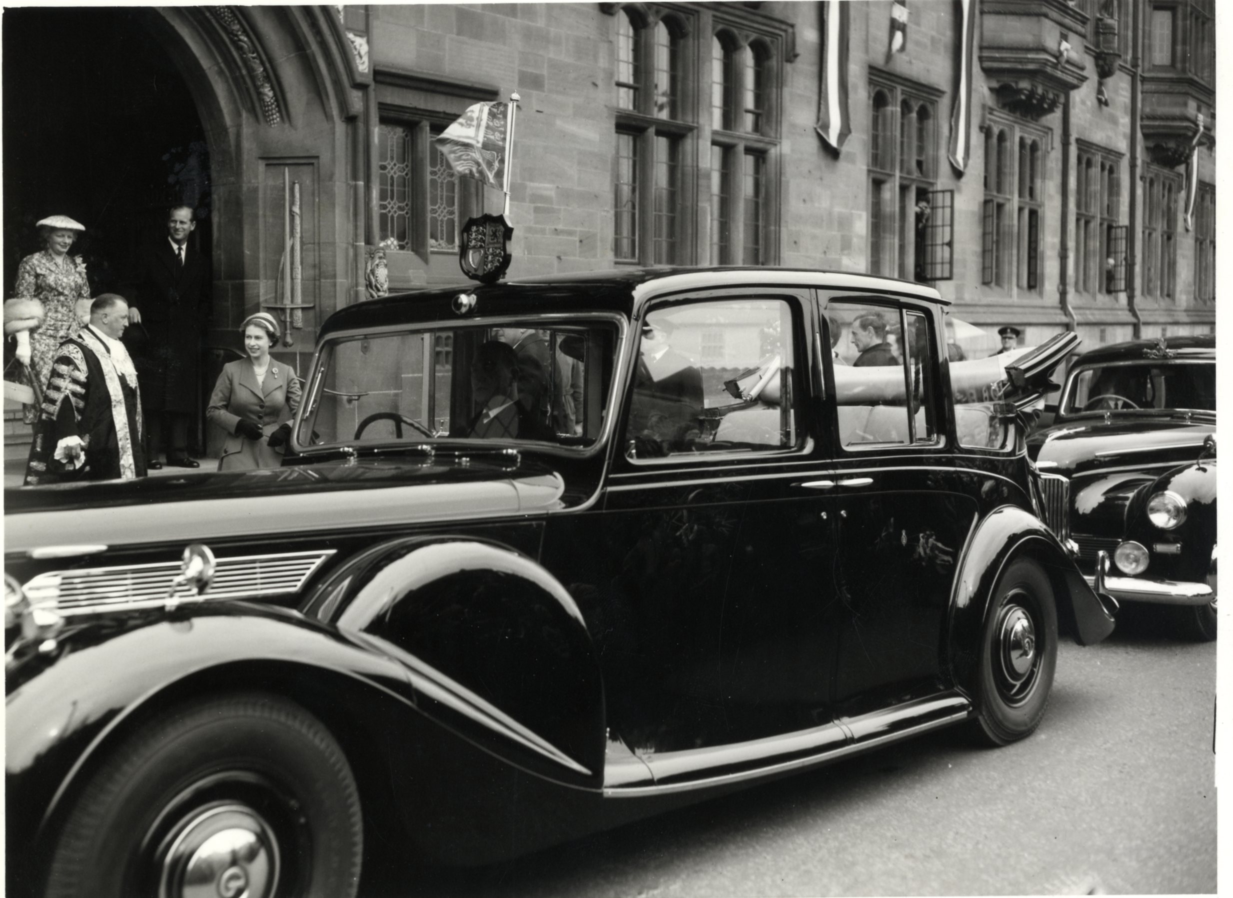 A photograph of Queen Elizabeth II leaving Coventry Council House in 1956, a car waiting outside to collect her