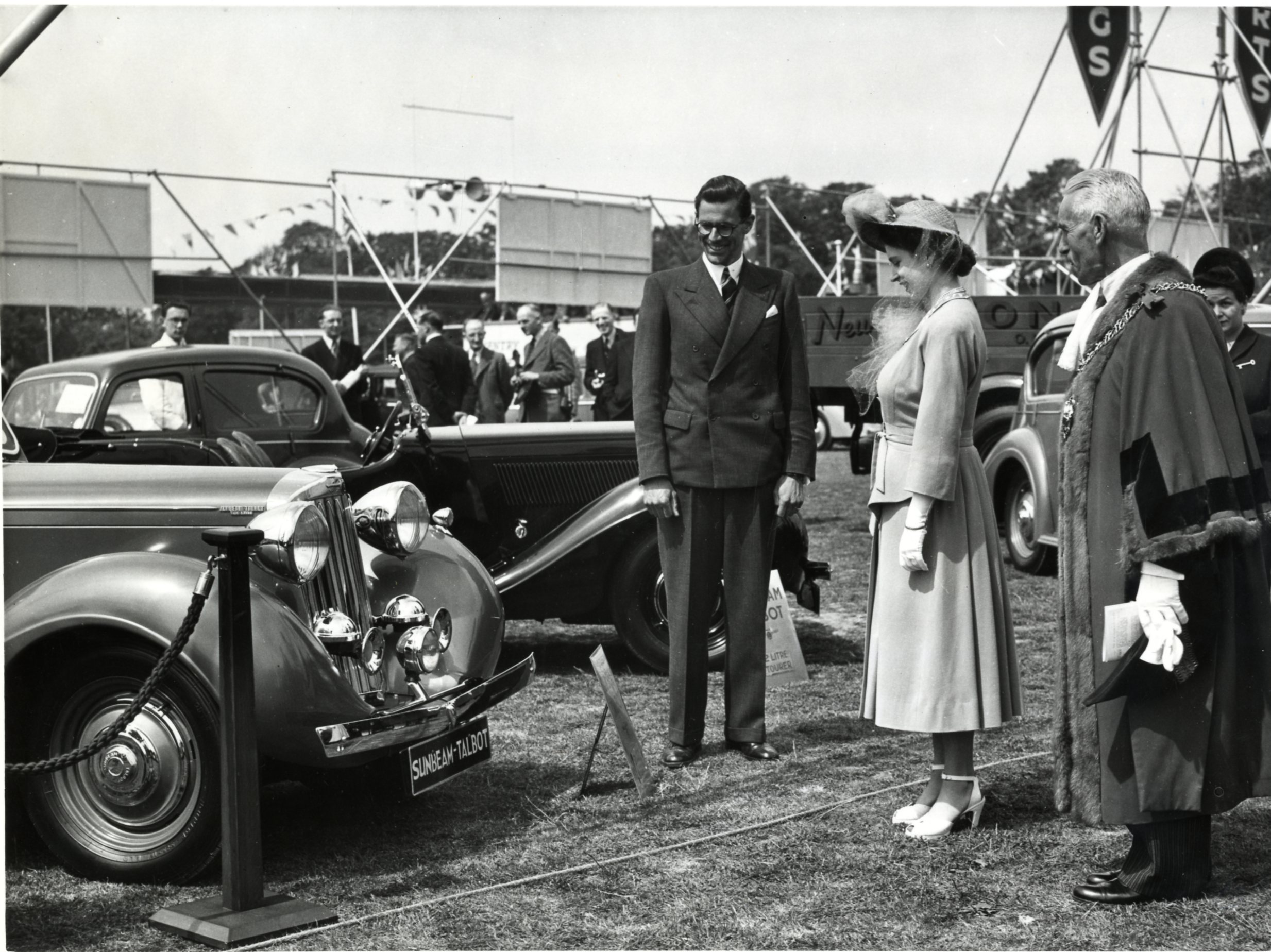 A black and white photo of Princess Elizabeth looking at a display of vehicles in the War Memorial Park, Coventry